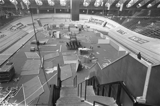 Großes Schwarz-Weiß-Foto eines beschädigten Stadioninneren mit verstreuter Trümmern, einigen anwesenden Personen und sichtbarer Decke.