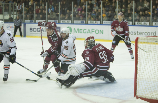 Gruppe von Menschen, die Hockey auf einem Eisstadion mit Tor auf der rechten Seite spielen, Helmträger mit Stöcken, Zuschauer auf Tribüne mit Bannern im Hintergrund.