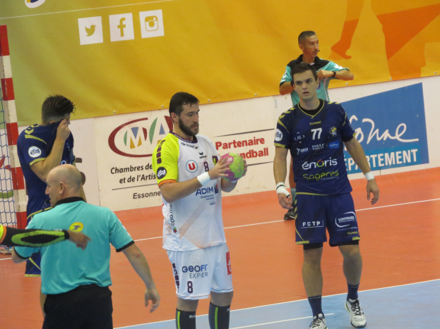 Eine Gruppe von Männern steht auf einem Futsal-Platz, einer hält einen Ball, mit einem Tor auf der linken Seite und Bannern im Hintergrund.