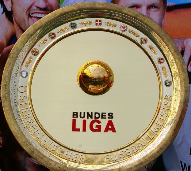 Goldener Schild mit 'Bundesliga'-Text, gehalten von einem Mann mit einem Banner im Hintergrund, das drei Personen zeigt.