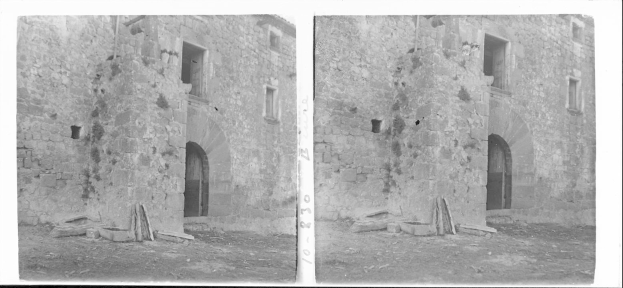 Schwarzes und weißtes Foto von den Ruinen eines alten Steinschlosses mit intakten Wänden, Fenstern und Bogengängen, umgeben von verstreuten Steinen und hölzernen Gegenständen.