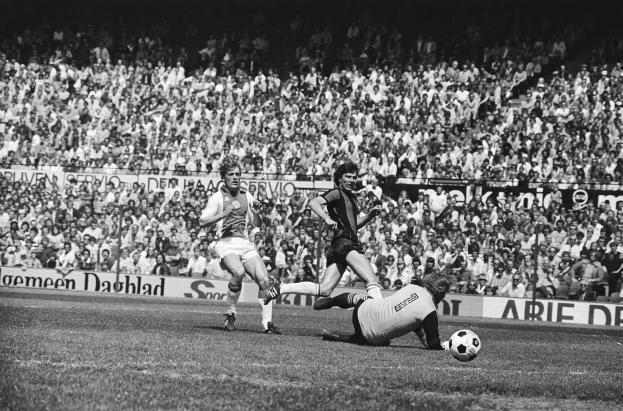 Schwarzes und weißes Foto von Männern, die auf einem Feld Füßball spielen, mit Zuschauern im Hintergrund und einem Bundesliga 1978-79 Ajax 1-1 Hannover 96-Banner.