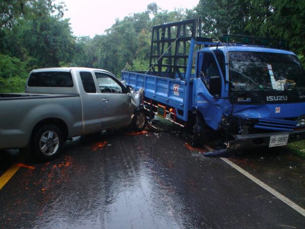 Ein schwerbeschädigtes Lkw mit eingedrückter Front und verbeulter Karosserie liegt auf der Seite einer Straße, umgeben von Bäumen unter einem klaren blauen Himmel.