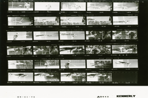 Schwarzes und weißes Foto eines konzentrierten Tennisspielers in einem weißen Hemd und Shorts, der einen Schläger hält, mit einem Filmstreifen im Hintergrund.