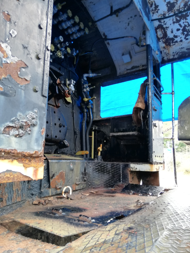 Innenansicht eines stark verrosteten und abgenutzten Truck-Cockpits mit Bäumen und einem klaren blauen Himmel durch das Heckfenster.