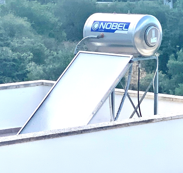 Solarwassererwärmer mit einem Speicherbehälter auf dem Dach eines Gebäudes montiert, Bäume im Hintergrund.