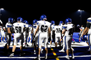 Eine Gruppe von Füßballspielern in Helmen und Stützen steht auf einem Feld unter Stadionflutlicht, bereit für ein Spiel.