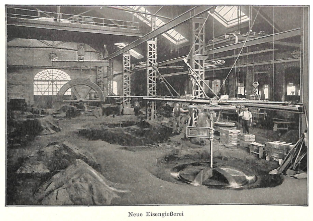 Schwarzes und weißes Foto einer Fabrikhalle mit Arbeitern, die Maschinen bedienen, umgeben von Metallstangen und -rohren, beschriftet mit 'Neue Eisenglebeerei, die erste Fabrik in Deutschland' unten.