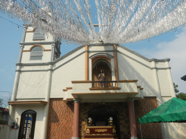 Weiße Kirche mit grünem Zelt davor, umgeben von Bäumen unter einem klaren blauen Himmel, mit dekorativen Gegenständen, die von der Kirchendecke hängen.