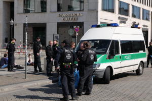 Polizisten vor einem Starbucks-Café mit einem Van auf der rechten Seite und Menschen auf der linken Seite, im Hintergrund ein Gebäude, ein Schild, eine Laterne und ein Zaun.