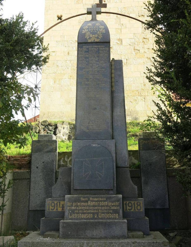 Denkmal vor einer Kirche mit einem Kreuz, umgeben von Bäumen und einer Mauer, gewidmet den deutschen Soldaten, die im Zweiten Weltkrieg starben.