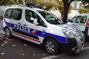 Ein Polizeiwagen mit einem sichtbaren Vorderrad ist auf einer von Bäumen und Gebäuden gesäumten Straße geparkt.