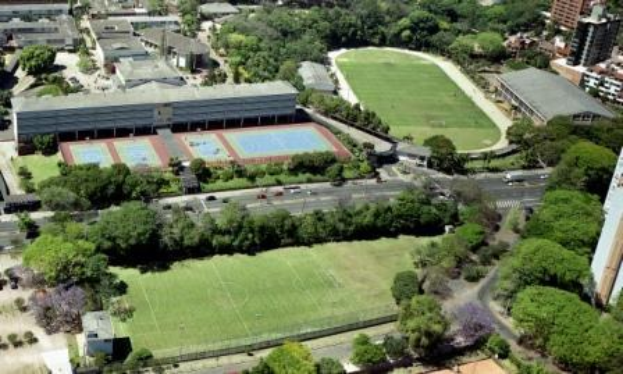 Luftaufnahme eines Fußballfeldes an der Universität Sydney, umgeben von Bäumen, Gebäuden und Fahrzeugen, mit einem neuen Sportkomplex im Bau.