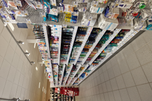 Eine Apothekenregal mit verschiedenen Medikamenten, die in Regalen angeordnet sind und von Deckenleuchten beleuchtet werden.