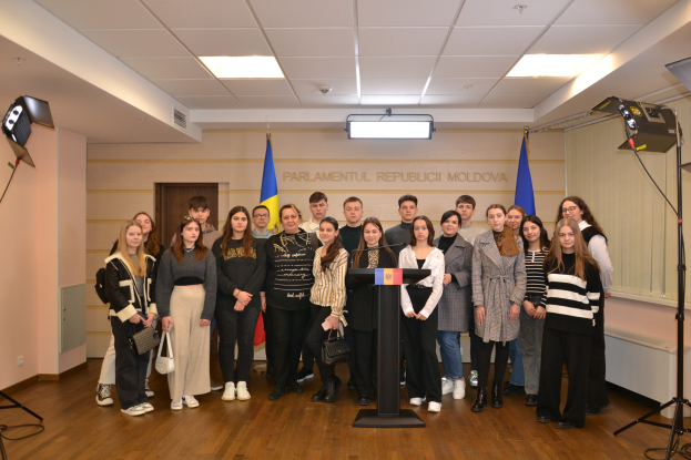Gruppe von Menschen auf einem Podium mit Mikrofonen, umgeben von Fahnen, einer Wand mit "Moldova Youth Congress 2018", einer Tür, Deckenleuchten und Scheinwerfern.