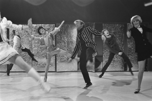 Eine Gruppe von Menschen, die auf einer Bühne tanzen, mit einer Wand im Hintergrund, alles in Schwarz-Weiß, mit Schuhen.