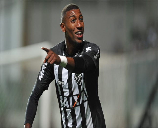 Fußballspieler in schwarzer und weißer gestreifter T-Shirt, der ein Tor feiert und lächelt, Hintergrund unscharf.