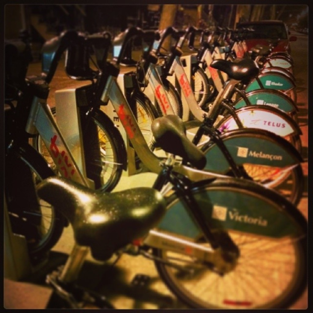 Mehrere Fahrräder sind in der Mitte des Bildes geparkt, hinter ihnen ist ein Fahrzeug sichtbar.