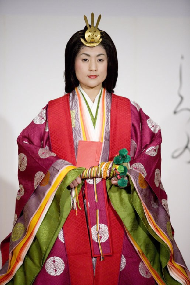 Eine Frau in einem traditionellen japanischen Kimono steht selbstbewusst auf einem Laufsteg und trägt ein leuchtend rotes und grünes Kleid mit aufwändigen Mustern und einem ordentlichen Dutt.