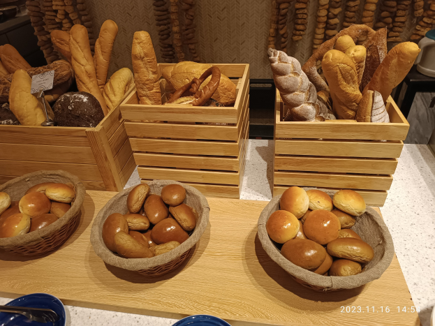 Holztisch mit Körben voller Brot, Tellern und Löffeln in einer Pariser Bäckerei mit einer gewässerten Wand im Hintergrund.
