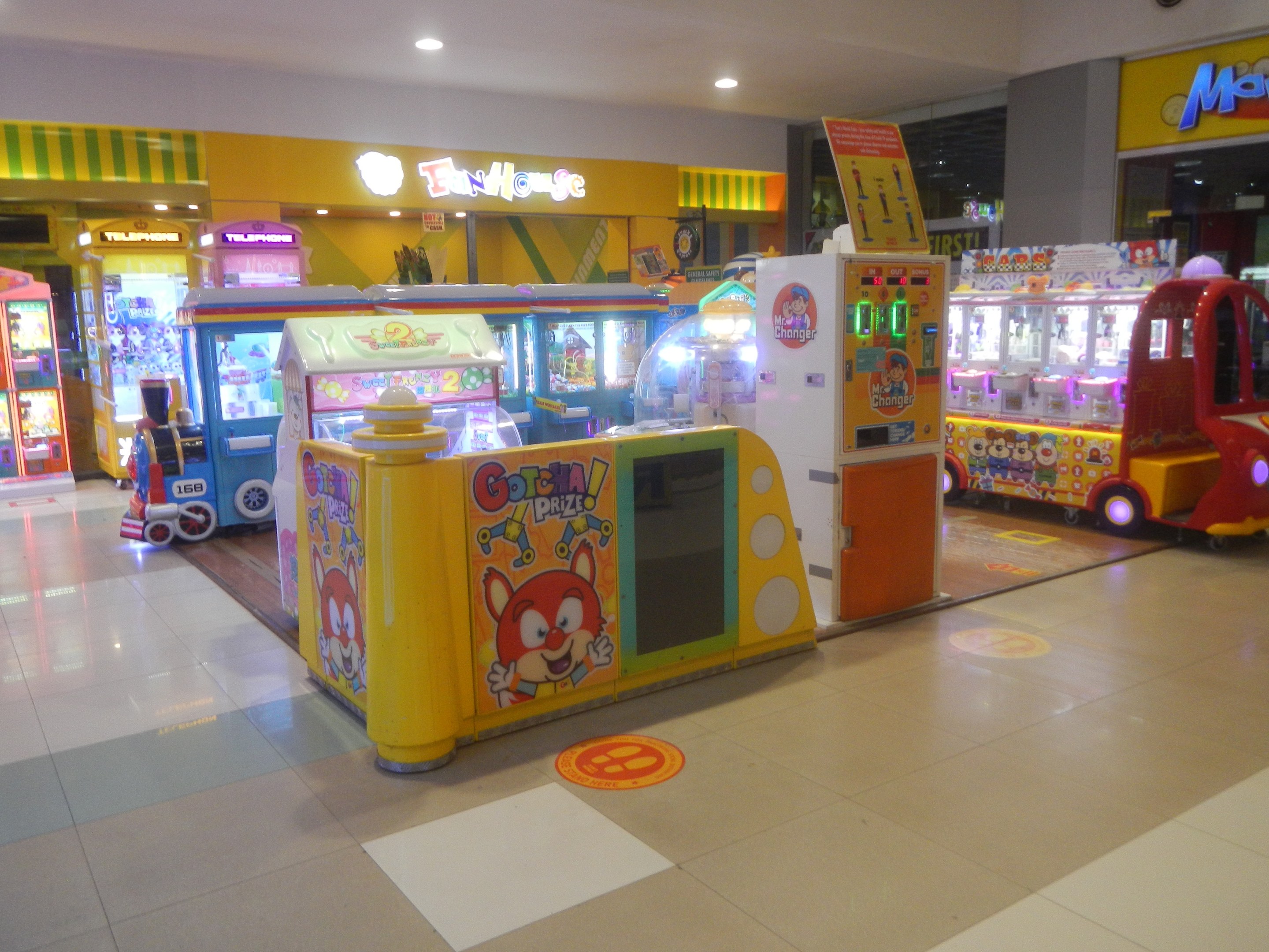 Ein geräumiger Arcade-Raum mit verschiedenen Arten von Arcade-Automaten, einer beleuchteten Decke und einer Rückwand in einer Vergnügungspark-Atmosphäre.