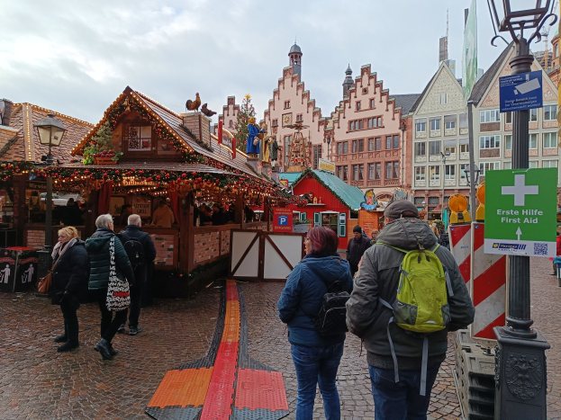 Menschen, die auf einem Kopfsteinpflasterweg neben einem Weihnachtsmarkt in Nürnberg, Deutschland, gehen, mit Laternenmasten und Informationsschildern im Vordergrund und Gebäuden im Hintergrund.