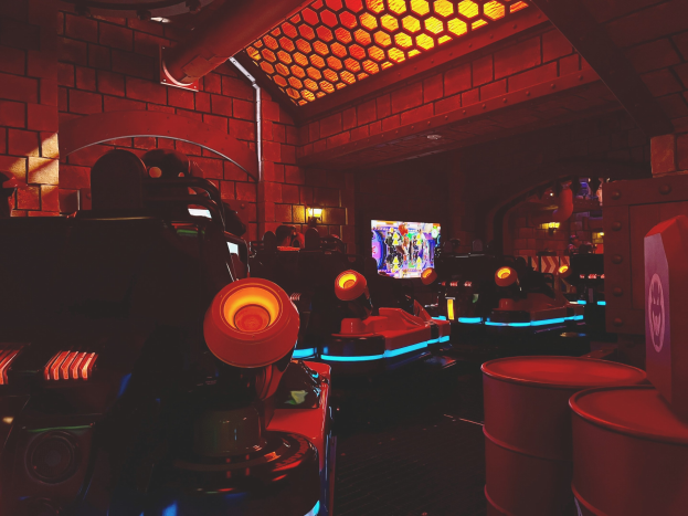 Ein hell erleuchteter Raum voller verschiedener Arcade-Videospielautomaten, Bildschirme und andere Gaming-Ausstattung, der eine energiegeladene Atmosphäre schafft.