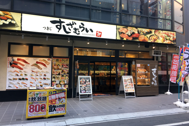 Außenansicht einer Sushi-Bar mit Glaswänden und -türen, die Speisekarten und beleuchtete Schilder zeigt, an einer Straßenecke in Tokyo, Japan.