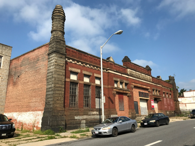 Alter Backsteinformer St. Louis Feuerwache mit seitlichem Schornstein, umgeben von Straßenlaternen, Fahrzeugen, Infotafeln, Bäumen und einem bewölkten Himmel.