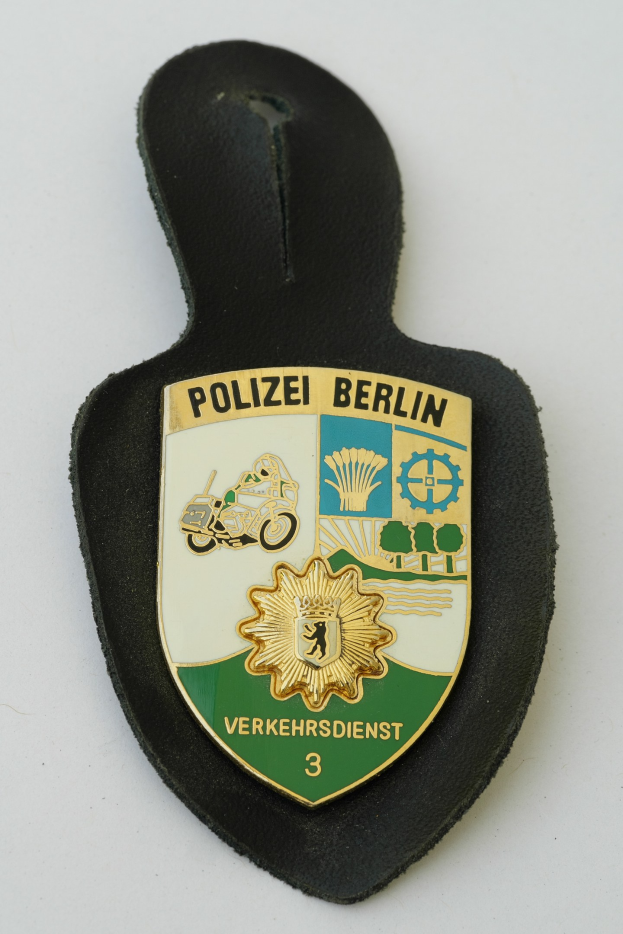 Ein schildförmiges Polizeibadge mit der Aufschrift "Polizei Berlin" auf einem blauen Hintergrund, einem weißen Rand und einem zentralen weißen Stern, das auf einer Oberfläche liegt.
