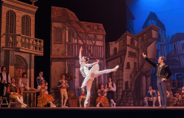 Zwei Tänzer performen auf der Bühne der Royal Opera House in London, mit einem Publikum im Hintergrund und einer projizierten Stadtkulisse.
