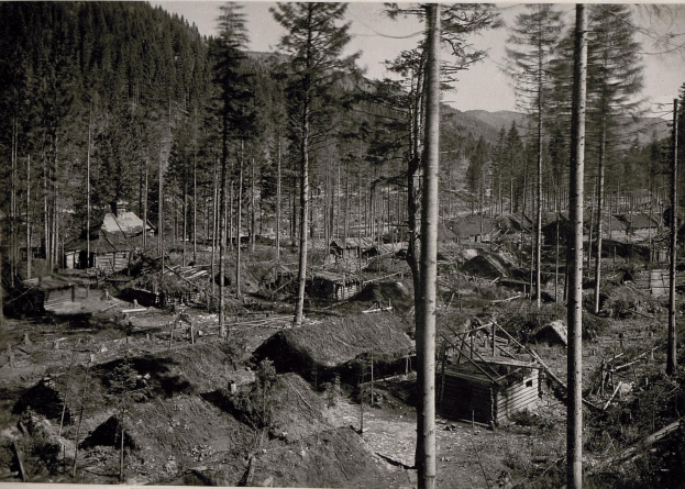 Schwarzes und weißes Foto eines kleinen Dorfes mit Hütten, Bäumen und Bergen im Hintergrund, mit Text unten.
