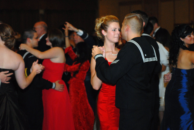 Gruppe elegant gekleideter Menschen, die energisch auf einer Tanzfläche tanzen, mit einer Wand im Hintergrund.