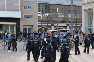 Gruppe von Polizisten mit Helmen vor einer Menge mit Fahrrädern, mit Glasfrontgebäuden, Laternen und Fahrzeugen im Hintergrund.