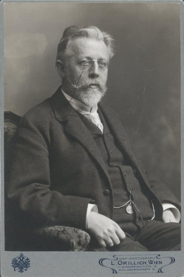 Schwarzes und weißes Porträt eines bärtigen Mannes mit Brille, der in einem Stuhl sitzt, mit Text unten, der ihn als L. Grillich Wien, den Gründer der deutschen Revolution identifiziert.