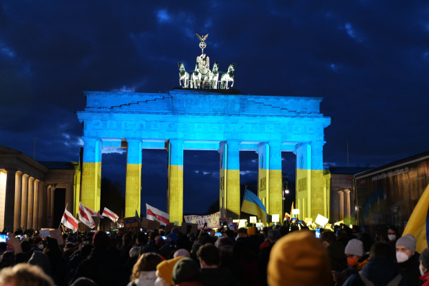 Menschenmenge mit Fahnen und Schildern vor dem Brandenburger Tor, mit einer Fahne auf der rechten Seite.