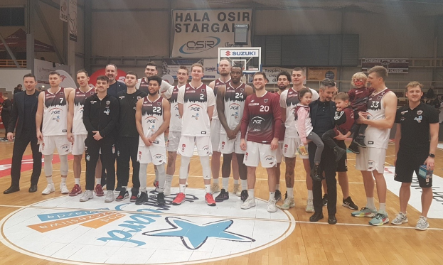 Eine Gruppe von Männern und Kindern auf einem Basketballfeld mit Schildern im Hintergrund, die "Hala Osir Starga" lesen.