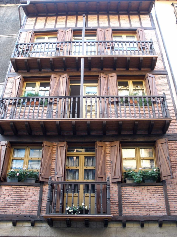 Ein mehrgeschossiges Gebäude mit zahlreichen Fenstern, Balkonen, Geländern, Türen und Blumenkübeln voller Pflanzen in Straßburg, Frankreich.