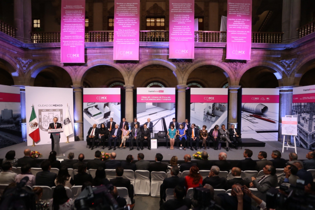 Eine Gruppe von Menschen auf einer Bühne mit einem Redner an einem Podium umgeben von Dekorationen während einer Pressekonferenz für CDMX.