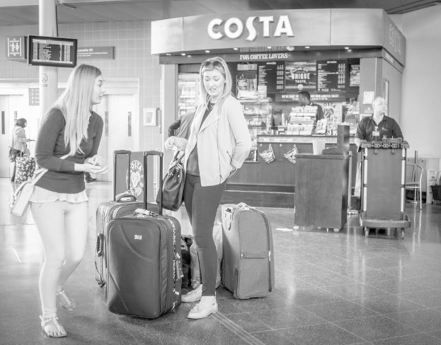 Zwei Frauen mit Gep√§ckst√ľcken vor einem Kaffeeschop, wahrscheinlich am Flughafen.