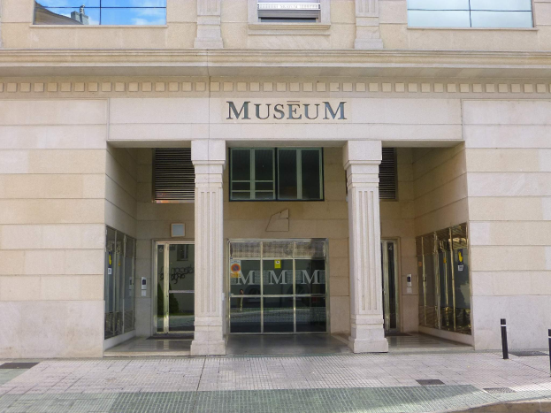 Gro├čes Geb├Ąude mit Glasfenstern und -türen, Pfeilern und Wandtext, mit einem Weg, der zur Museumseintrittsstelle führt.