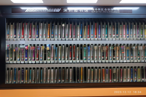 Eine Bibliothek mit hohen Bücherregalen, beleuchtet von Deckenlampen, mit einer Texttafel und einem Wasserzeichen unten.