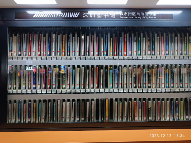 Eine Bibliothek mit hohen Bücherregalen, beleuchtet von Deckenlampen, mit einer Texttafel und einem Wasserzeichen unten.