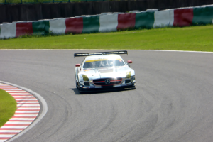 Ein Mercedes-Benz SLS AMG GT3 steht auf einer Straße am Nürburgring, umgeben von grünem Gras und einem Zaun im Hintergrund.