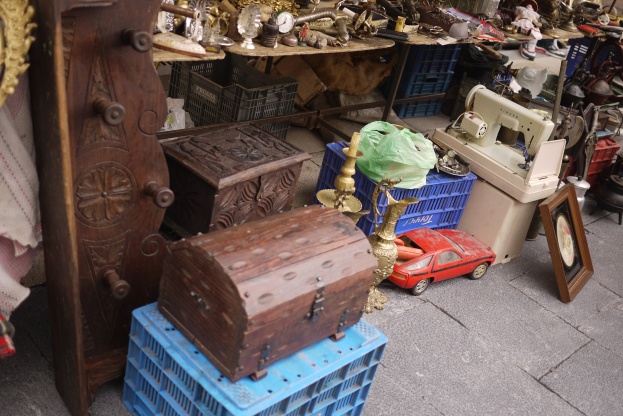 Ein Flohmarkt mit Holzkisten, einem Spielzeugauto, einer Nähmaschine, einem Foto Rahmen, einer Uhr und anderen Gegenständen auf Tischen.