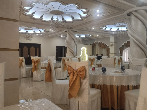 Ein großer Festsaal mit Tischen und Stühlen, die mit Dekorationsstoffen drapiert sind, umgeben von Türen und Vorhängen und beleuchtet von Kronleuchtern und Lichtern.