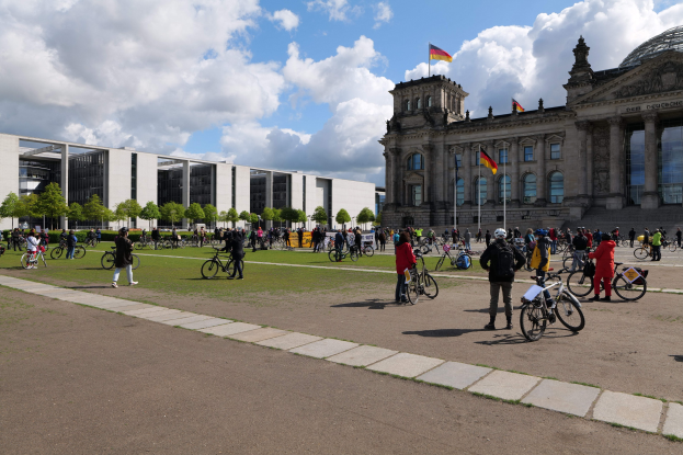 Menschen auf Fahrrädern vor dem Reichstaggebäude in Berlin, Deutschland, mit Flaggen und Säulen im Hintergrund.