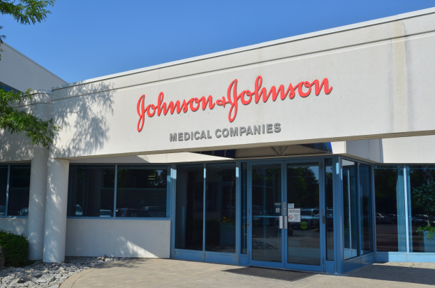 Außenansicht des Johnson & Johnson Medical Companies-Gebäudes mit Glaswänden und -türen, lesbarer Text an der Wand, dekorative Steine, Pflanzen und ein Baum auf der linken Seite, unter einem klaren blauen Himmel.