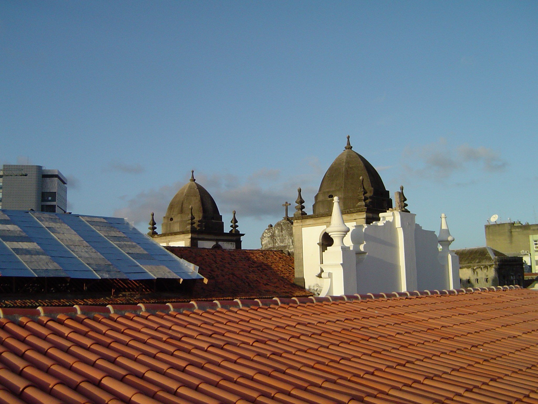 Stadtlandschaft mit Gebäuden im Vordergrund, einem blauen Himmel im Hintergrund und Solarpanels auf einem Dach.