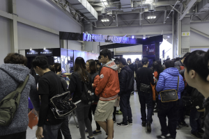 Eine Gruppe von Menschen vor einer Menge an einer Gaming-Messe, mit Schildern, Lichtern und Rohren im Hintergrund.